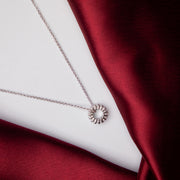 A silver-colored sundial pendant chain with embellished gemstones on a red velvet surface.